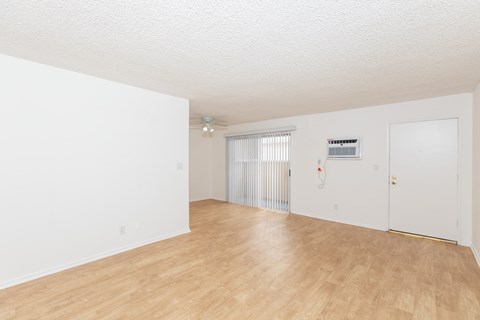 the living room and dining room of an apartment with wood flooring and white walls