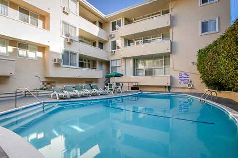 a swimming pool in front of a building with chairs and a resort style pool