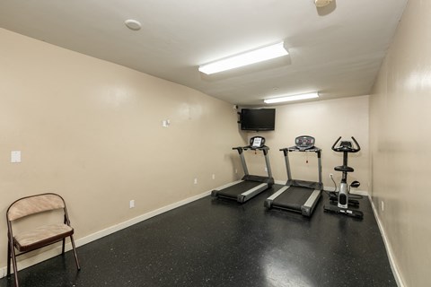 two treadmills and a chair in a gym room with a tv