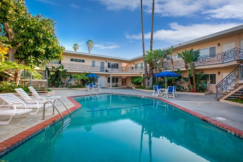 a swimming pool with chairs and umbrellas in front of a hotel