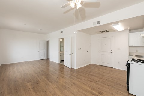 an empty living room with a kitchen and a ceiling fan