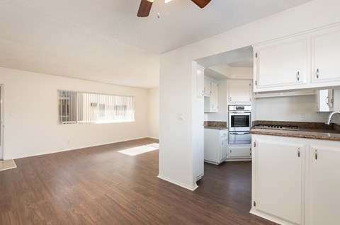 an empty kitchen and living room with white cabinets and wood floors