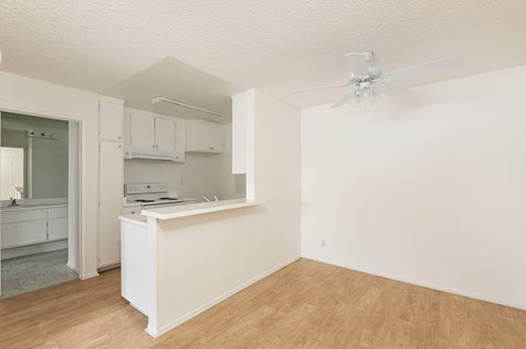 an empty living room with a kitchen and a ceiling fan