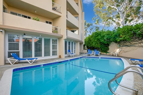 a swimming pool with chairs and a building in the background