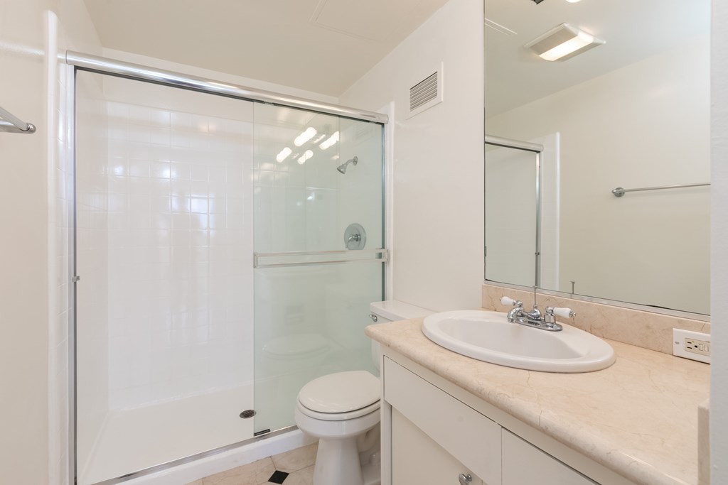 A bathroom with a toilet, sink, mirror, and shower.