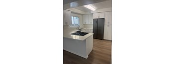 A kitchen with wood flooring, white cabinets and a black fridge.