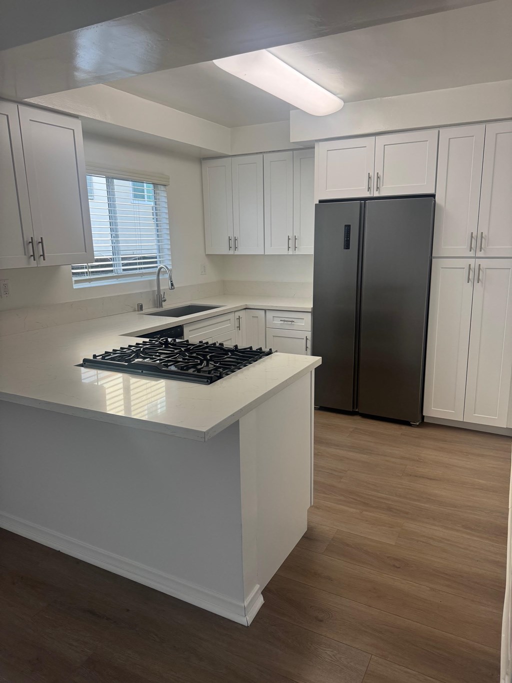 A kitchen with wood flooring, white cabinets and a black fridge.