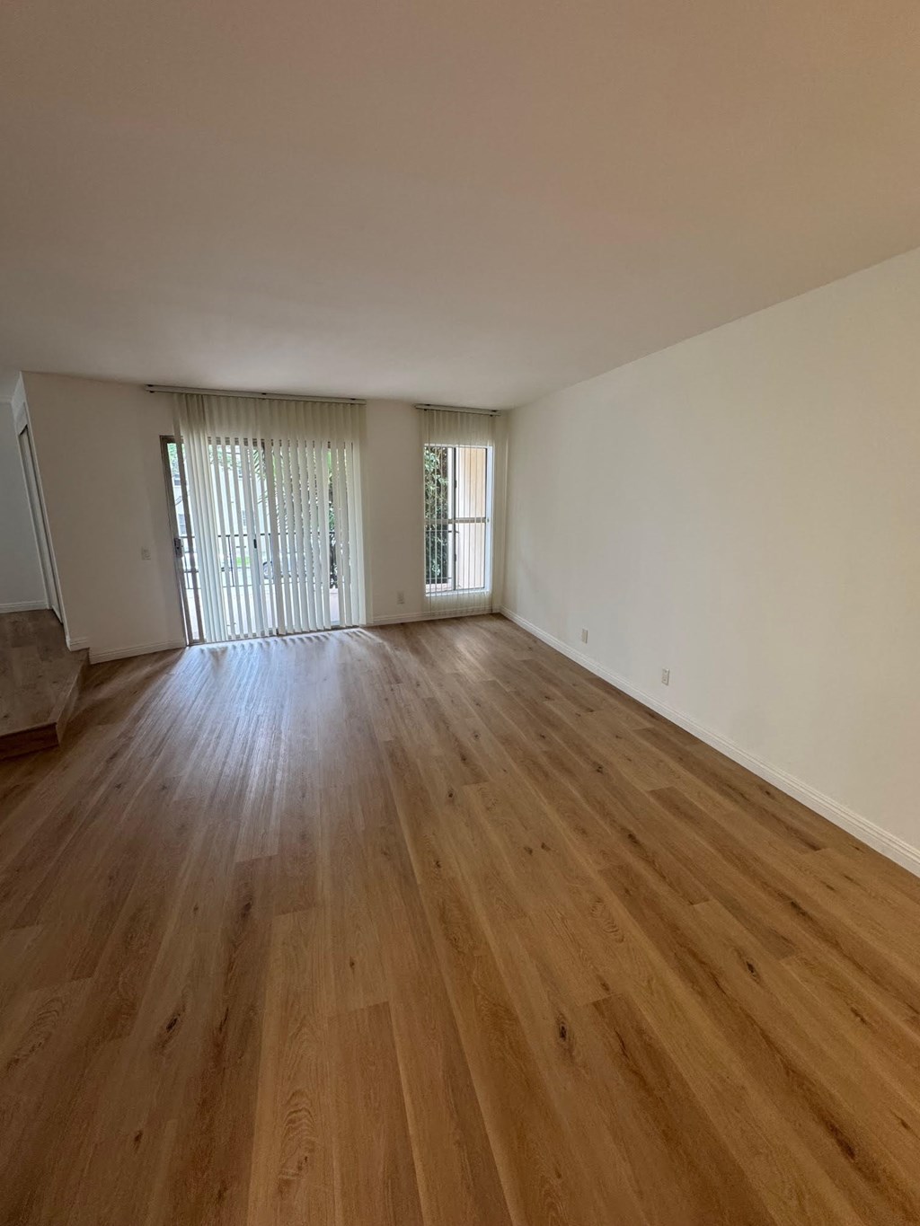 Living room with wooden flooring and two windows.