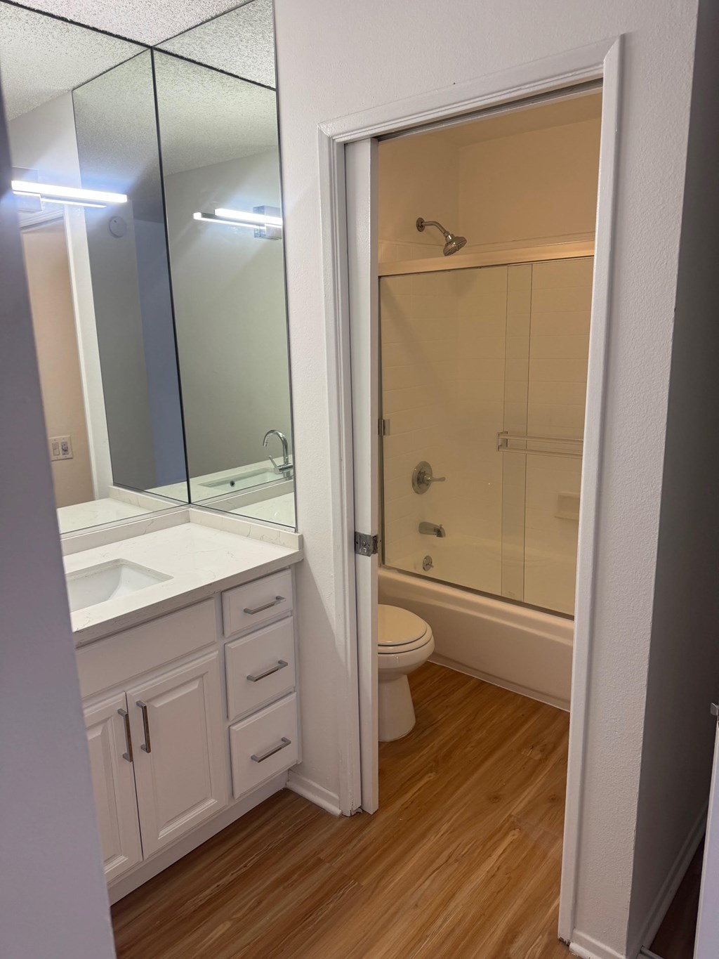 A white bathroom with a wooden floor and a glass shower stall.