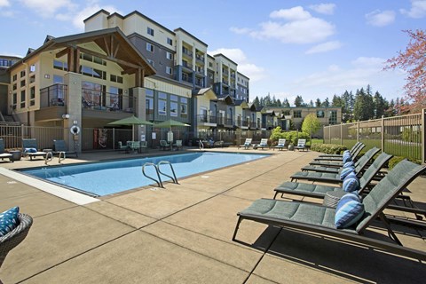 A large swimming pool surrounded by sun loungers in front of apartment buildings.