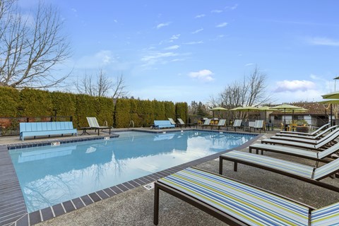 A large outdoor swimming pool with a bench and a striped table.