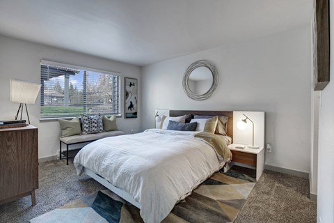 A bedroom with a large bed and a window overlooking a green area.