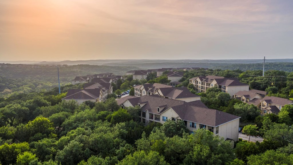 a neighborhood of houses surrounded by trees with a sunset in the background at The Verandah, Austin, 78726
