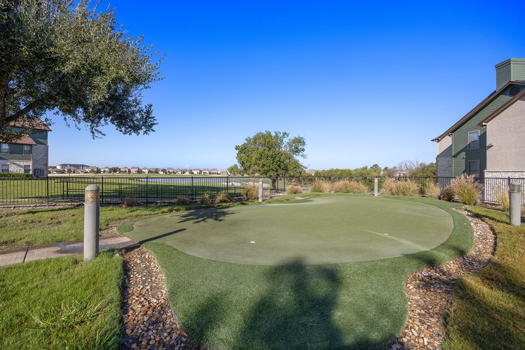 a putting green with a house and trees in the background at The Fairways at Star Ranch, Hutto, Texas