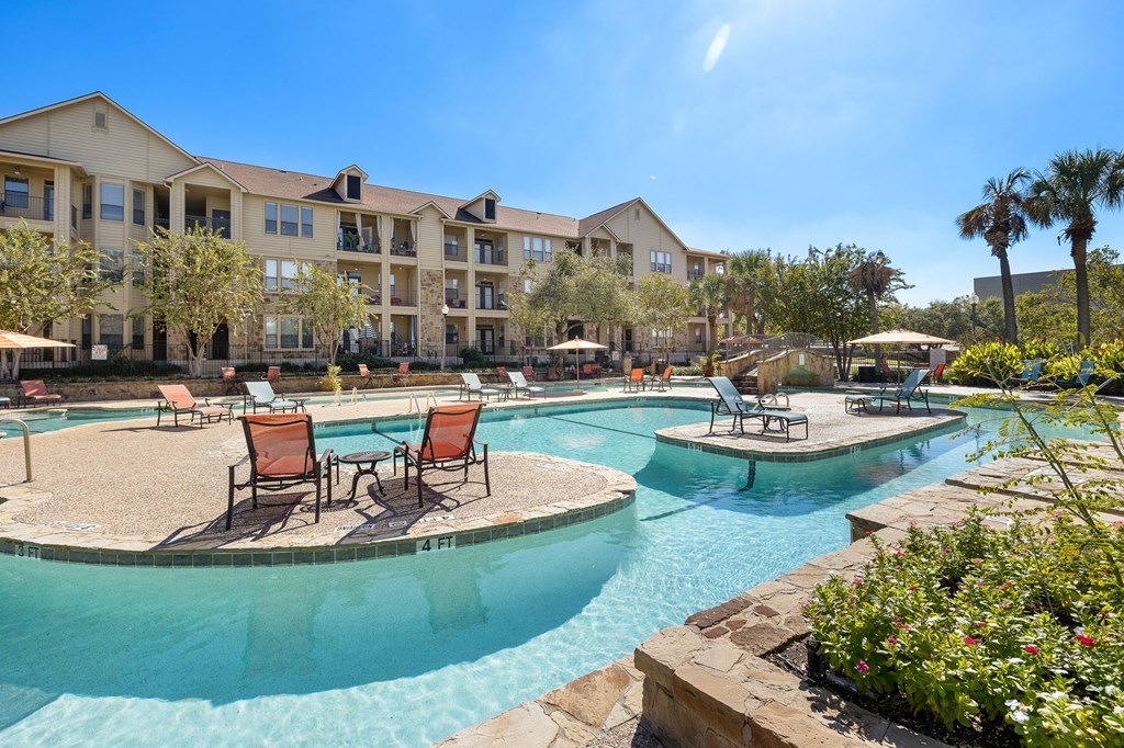 a swimming pool with chairs and tables in front of an apartment building at The Verandah, Texas, 78726