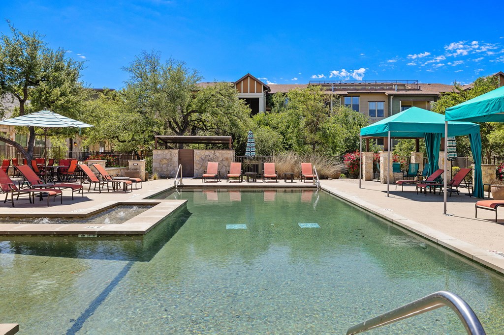 a swimming pool with chairs and umbrellas and a building in the background at Lakeline East Apartments, Texas, 78613
