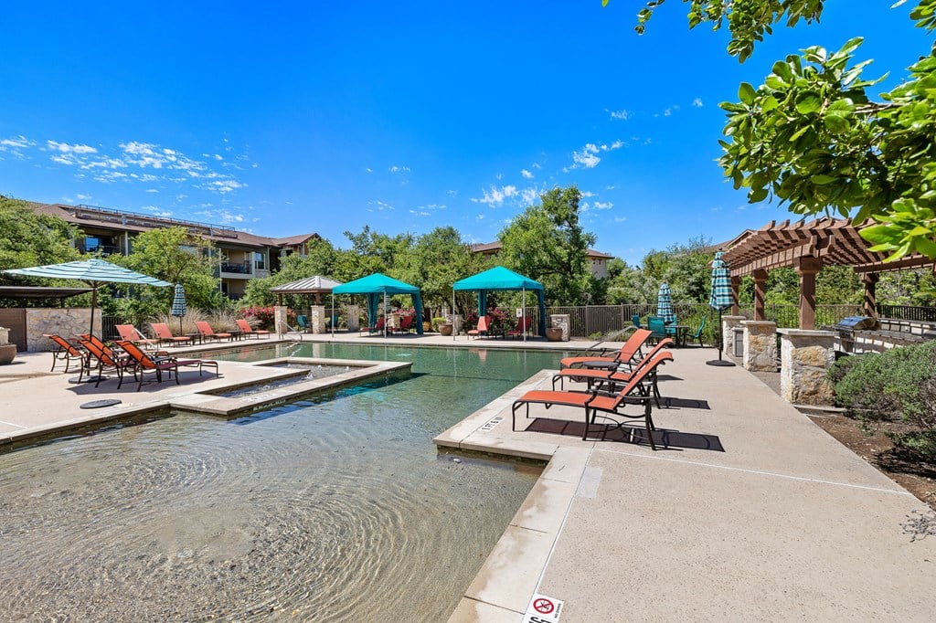 a swimming pool with chairs and umbrellas in front of a house at Lakeline East Apartments, Cedar Park, TX