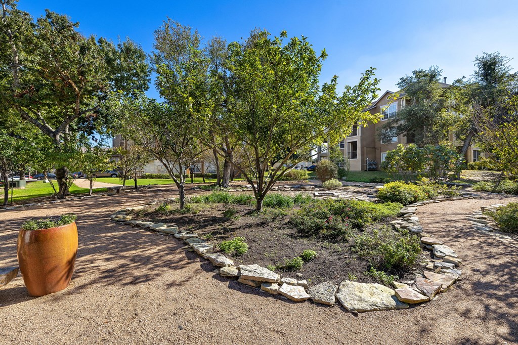 a garden with trees and rocks and a building in the background at Sonterra Apartment Homes, Austin, TX