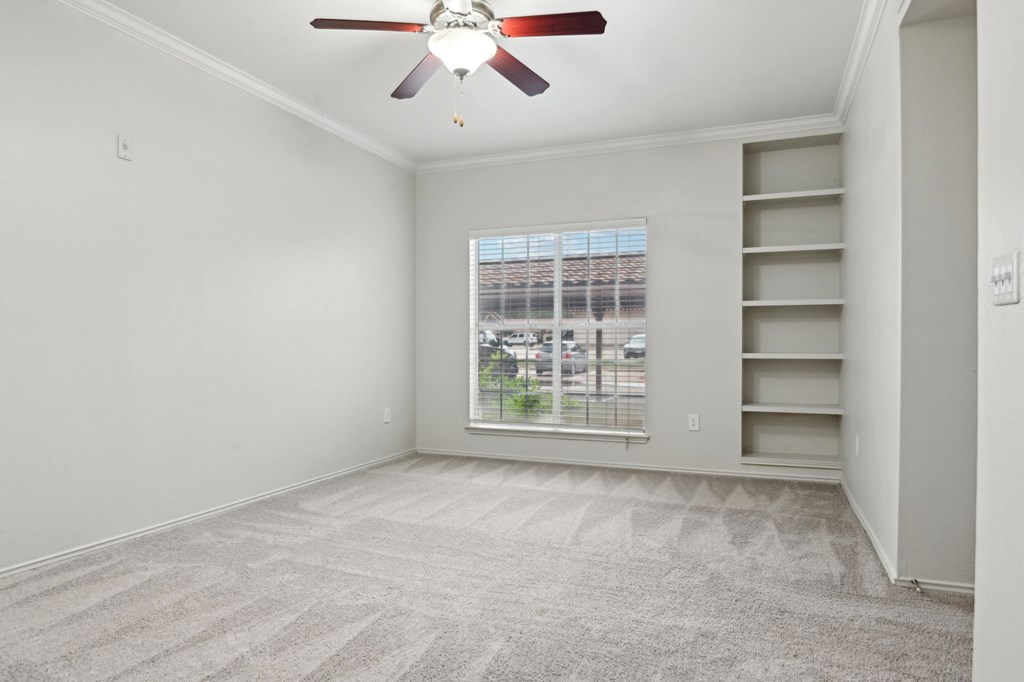 A room with a ceiling fan and a window overlooking a parking lot.