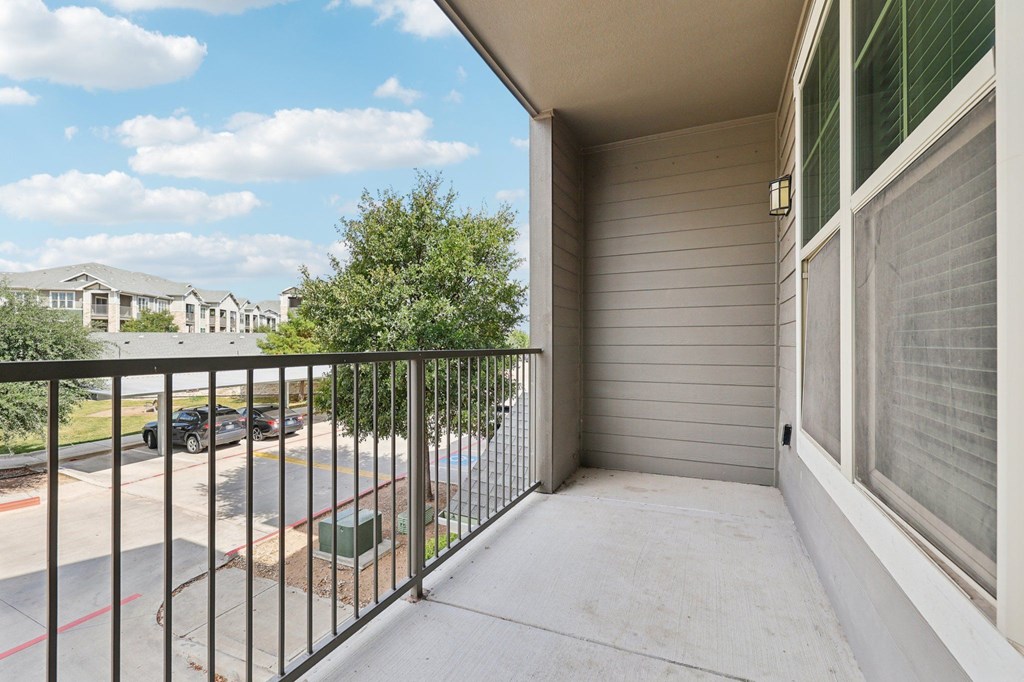 A balcony with a metal railing overlooks a parking lot and houses.
