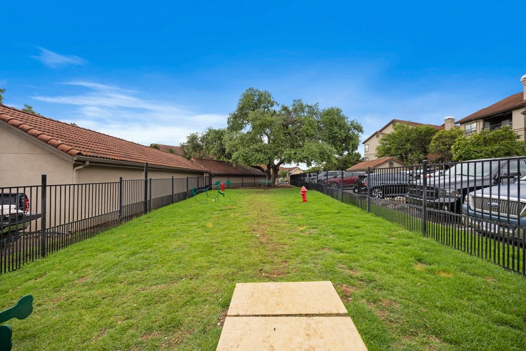 a large yard with a fence and cars in the parking lot at Waters Edge Apartment Homes, Texas