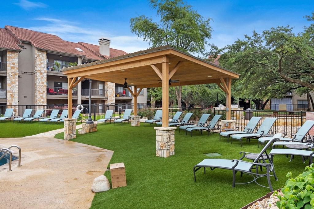 a pavilion with chaise lounge chairs on a grassy area with trees in the background at Waters Edge Apartment Homes, Texas, 78626