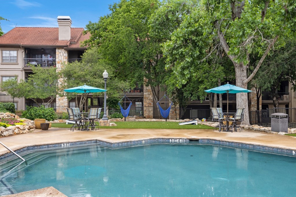a swimming pool with umbrellas and chairs next to a building at Waters Edge Apartment Homes, Texas, 78626