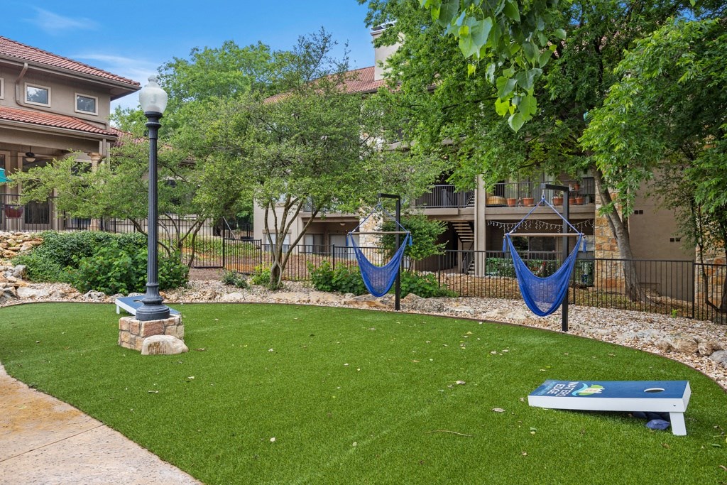 a yard with two hammocks and a seesaw in front of a building at Waters Edge Apartment Homes, Georgetown, 78626