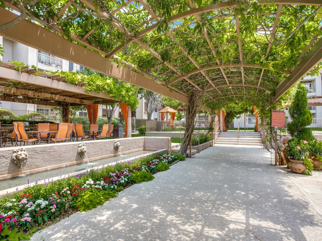 a courtyard with a pergola and flowers and benches at La Ventura Apartments, Plano, 75093