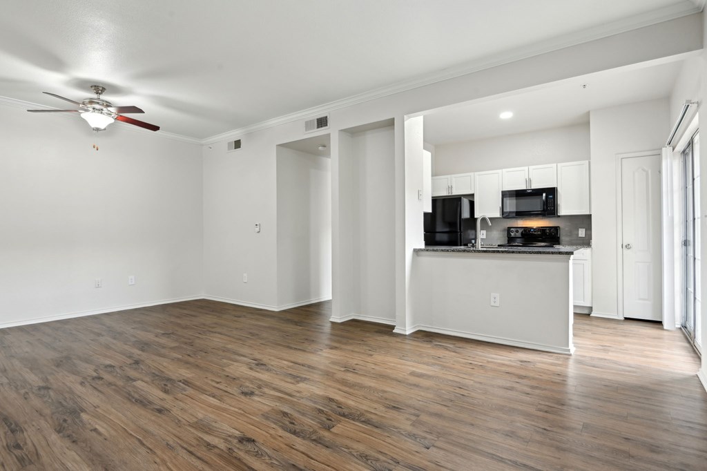 A room with a ceiling fan and a kitchen area with a microwave, oven, and refrigerator.