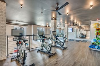 A gym with a row of exercise bikes and a fan. at Aurora Watson Branch, Mansfield, Texas