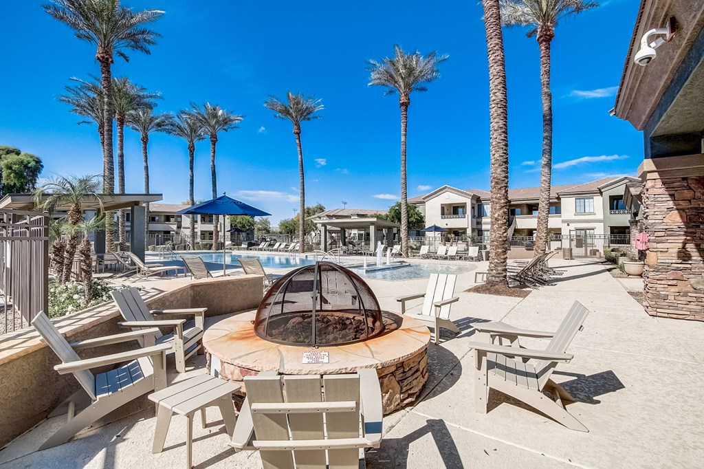 a fire pit with chairs around it near a pool with palm trees  at Adiamo Palm Valley, Goodyear, AZ
