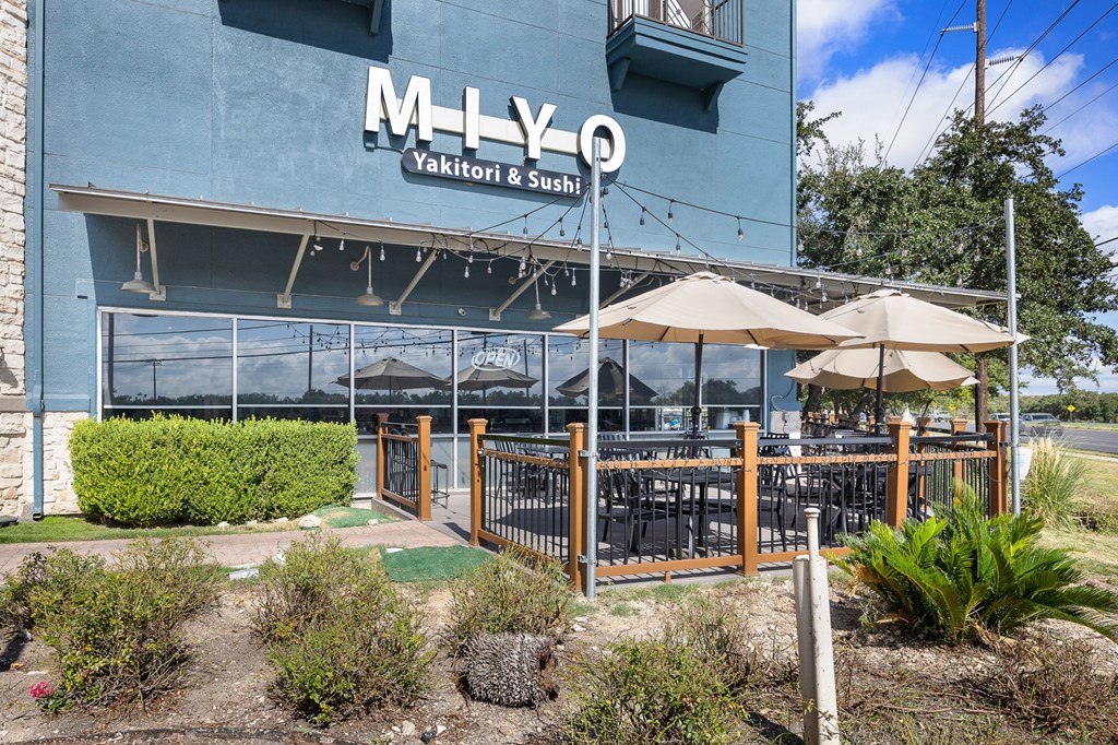 an outdoor patio with umbrellas and tables in front of a blue building at Artisan Apartments & Shops, Texas