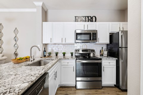 a white kitchen with stainless steel appliances and granite counter tops