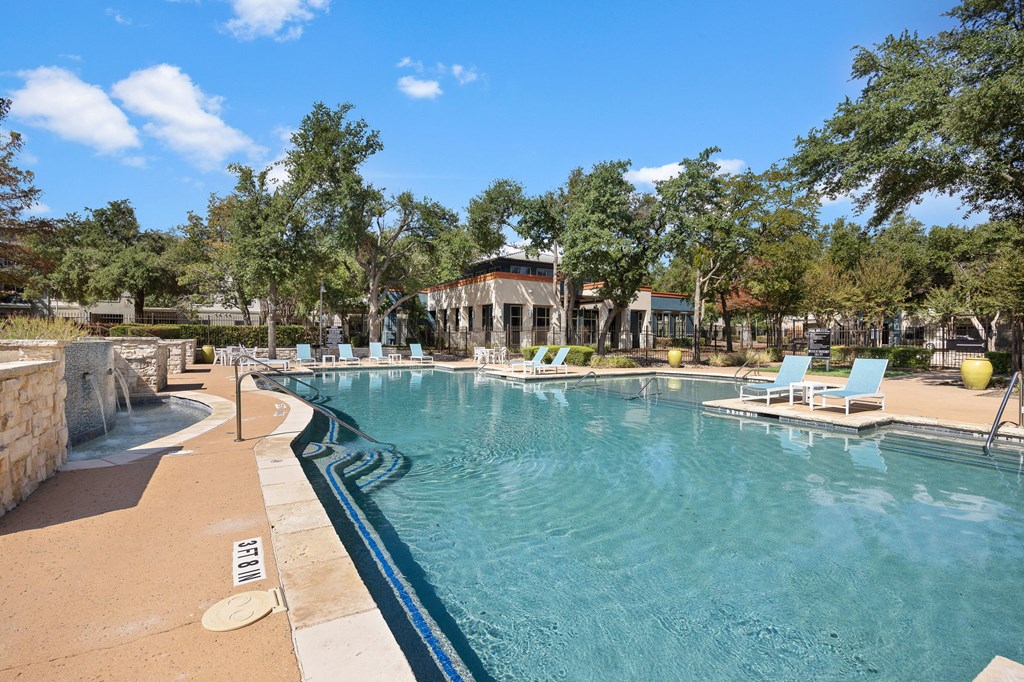a resort style pool with lounge chairs and trees in the background at Artisan Apartments & Shops, Austin, TX