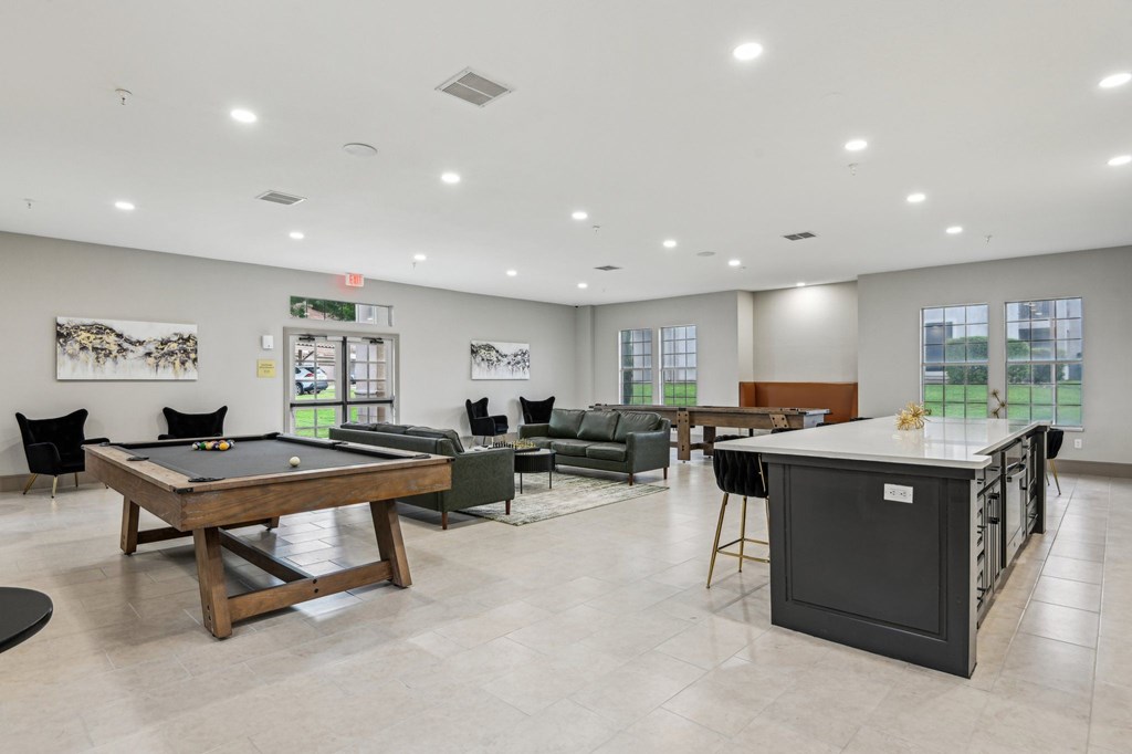 A billiard table is in the middle of a room with a pool table, a couch, and a bar.