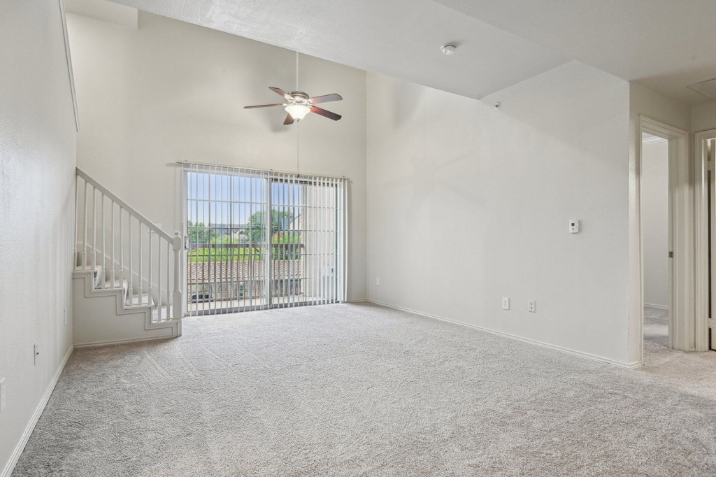 A room with a ceiling fan and a window with a view of a fence and trees.