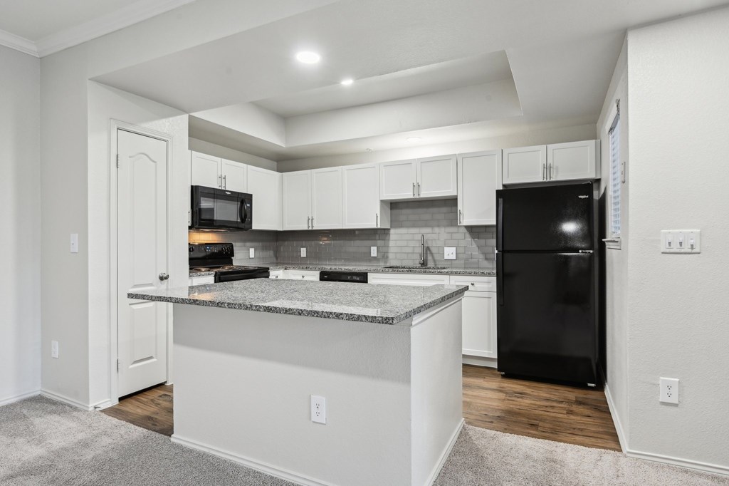 A kitchen with a black refrigerator and white cabinets.
