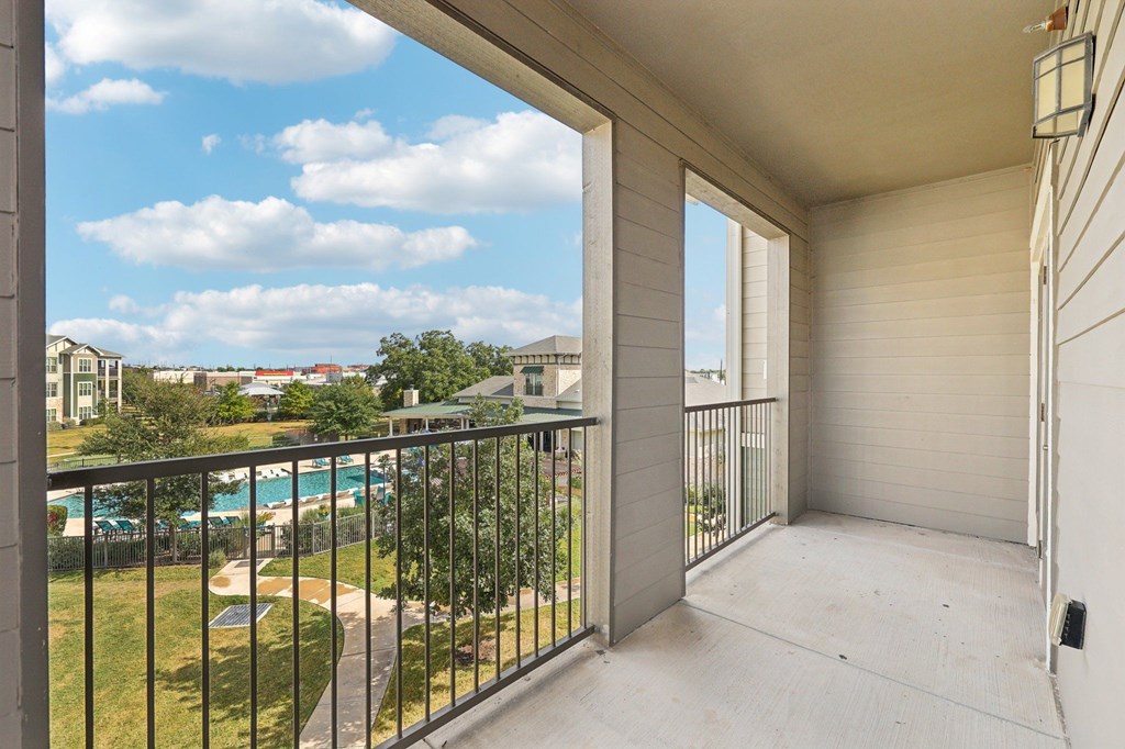 A balcony with a black railing and a pool in the distance.