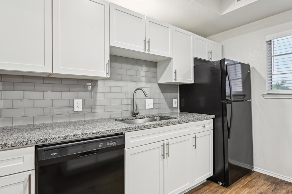 A kitchen with white cabinets and a black refrigerator.