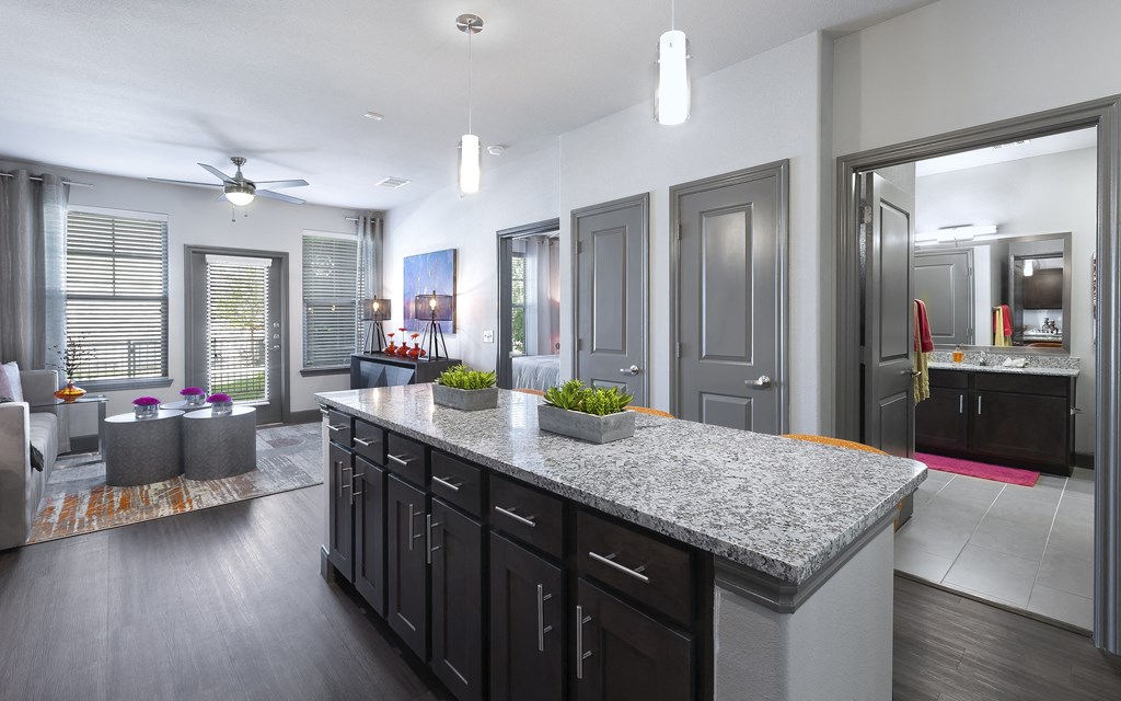 a kitchen with a granite counter top in front of a living room at North Creek, Hutto, TX