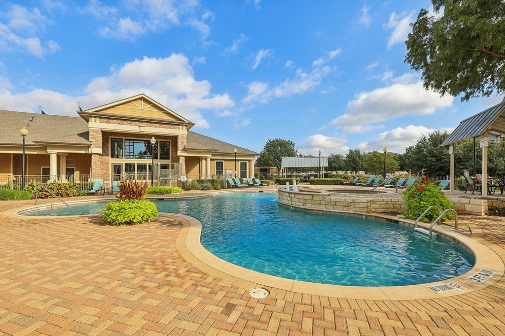 A large outdoor swimming pool surrounded by a brick patio.