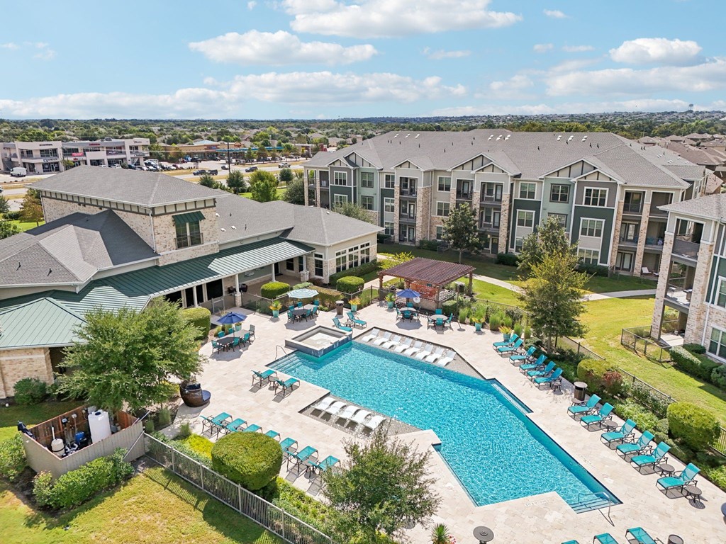 A large swimming pool surrounded by lounge chairs and umbrellas is the centerpiece of a resort-style outdoor area.
