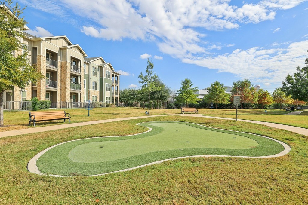 A park with a green lawn and apartment buildings in the background.
