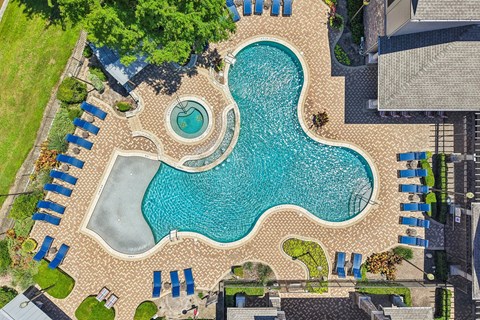 An aerial view of a swimming pool surrounded by a brick patio and blue lounge chairs.