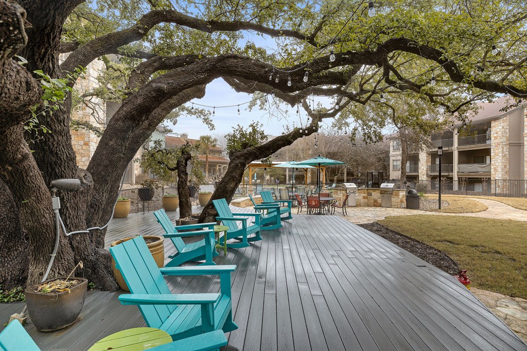a group of blue chairs sitting on a wooden deck under a tree at Waters Edge Apartment Homes, Georgetown