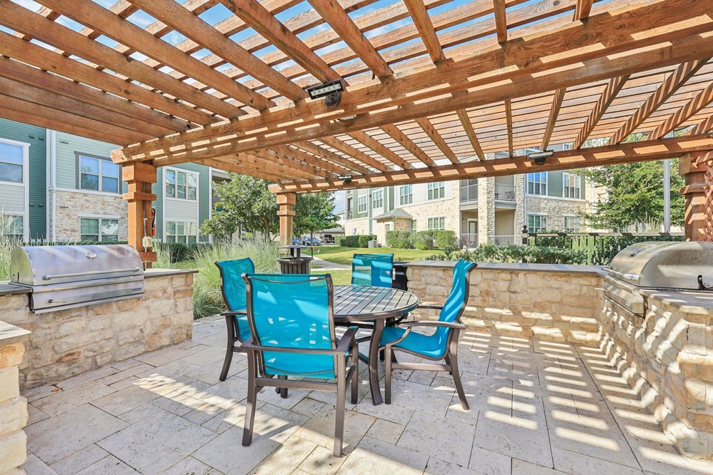 A wooden pergola with a table and chairs is set up on a patio.
