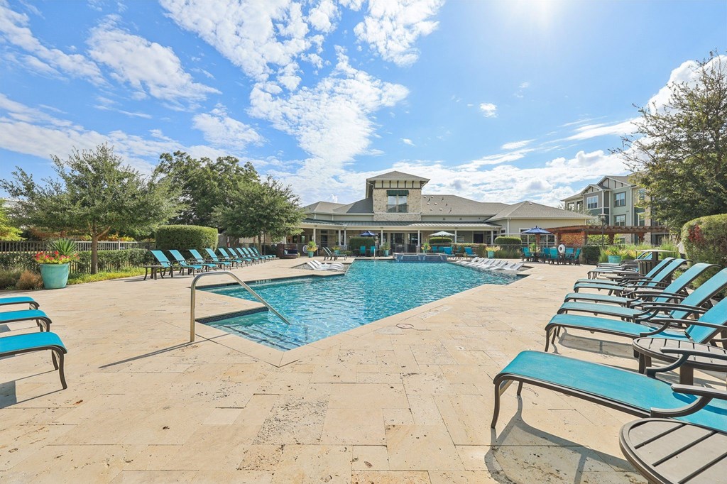 A sunny day at the pool with lounge chairs and a building in the background.