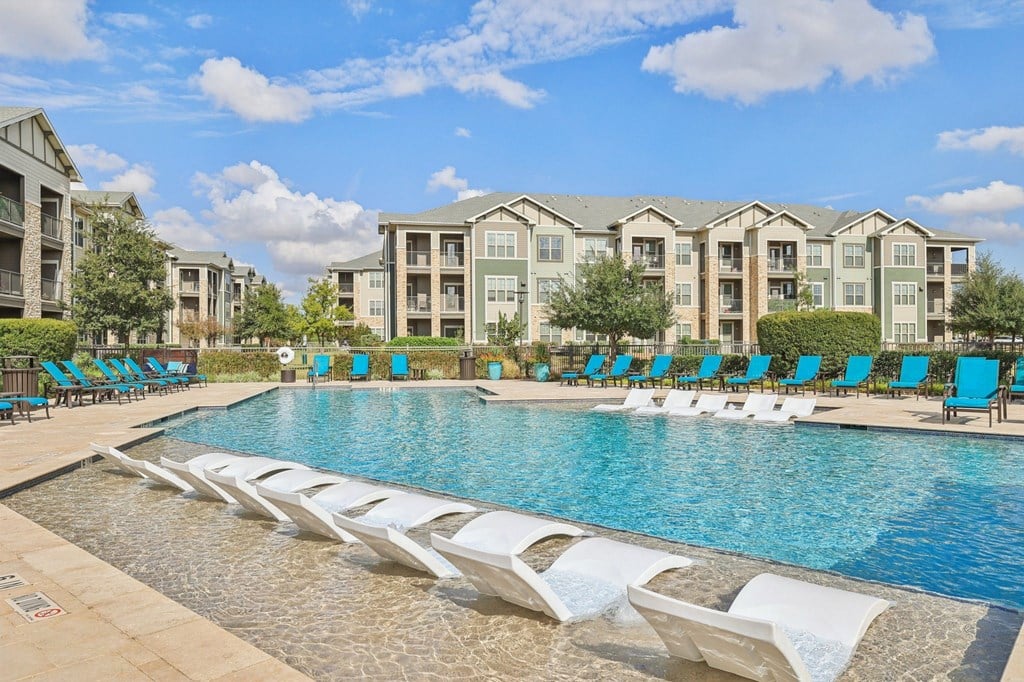 A swimming pool with lounge chairs and apartment buildings in the background.