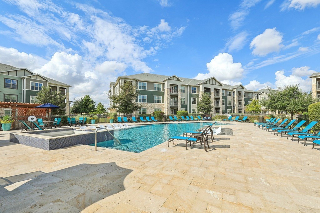 A large swimming pool surrounded by lounge chairs in front of apartment buildings.